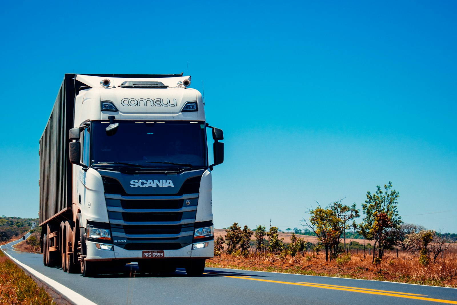Modern white transport truck travelling on an open highway under a clear blue sky